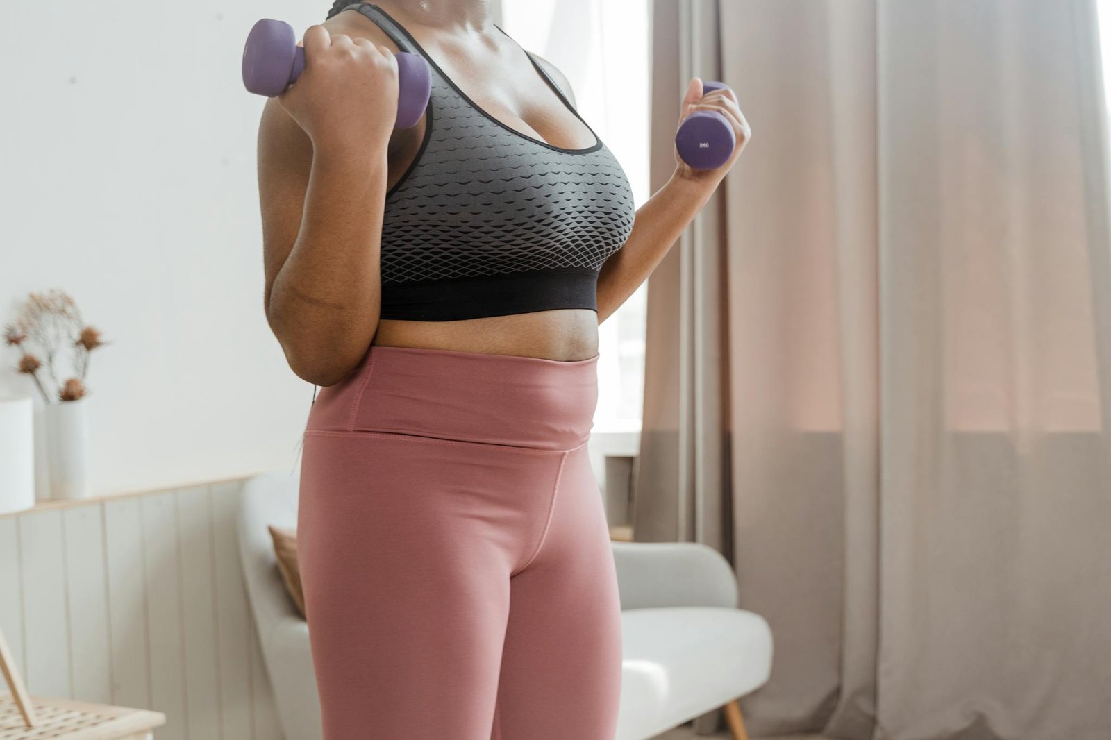 A woman in activewear working out indoors with dumbbells for fitness and wellness.